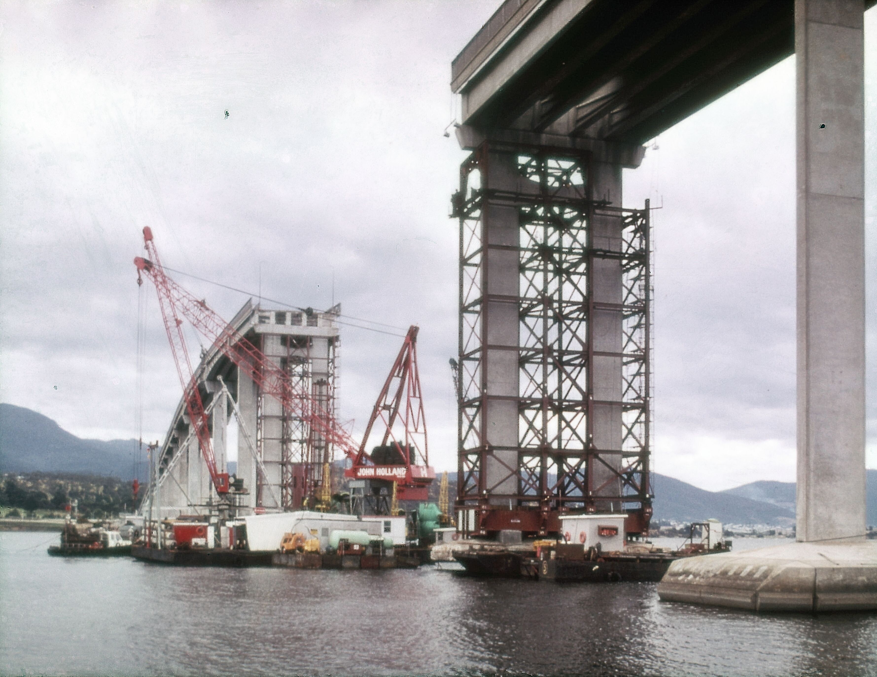A missing bridge span with cranes and barges working nearby.