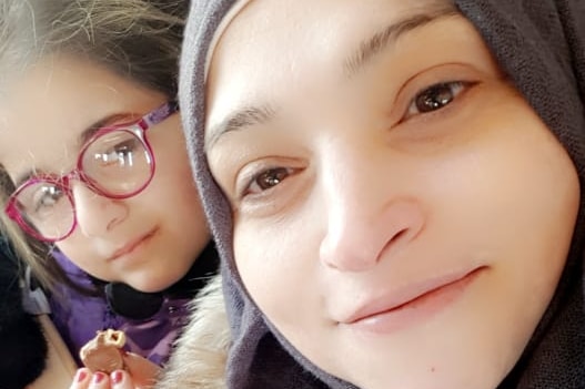 A woman in a headscarf and a little girl wearing glasses smile at the camera.