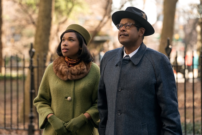 Set against park greenery, Jennifer Hudson in an olive coat and Forest Whitaker in dark grey look skyward.