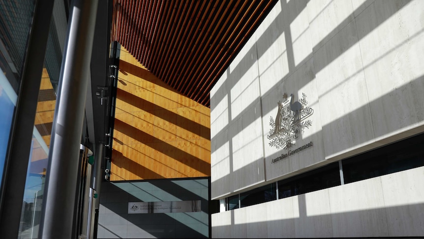 Geometric lines and shadows in entrance of building made of concrete and wood panelling.