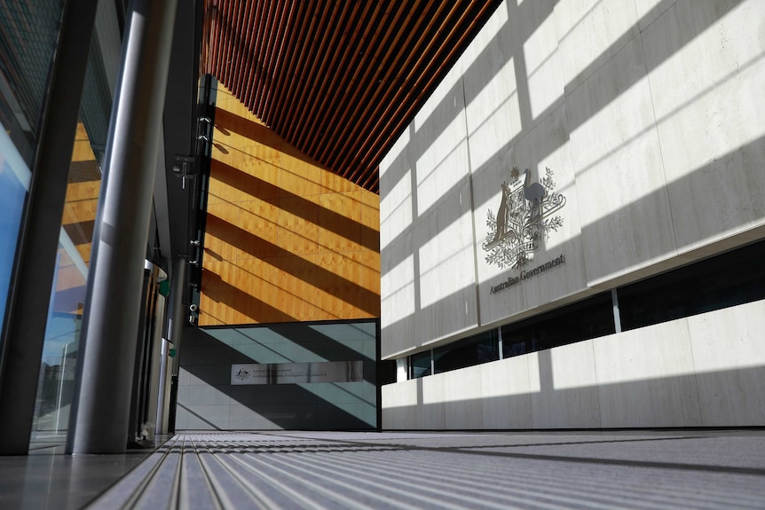 Geometric lines and shadows in entrance of building made of concrete and wood panelling.