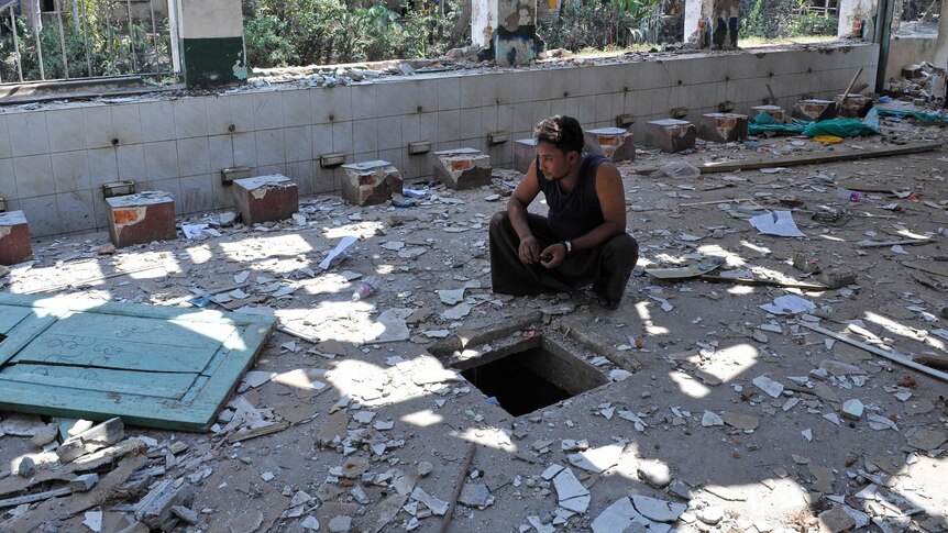 Myanmar, a man sits among the debris of a destroyed mosque