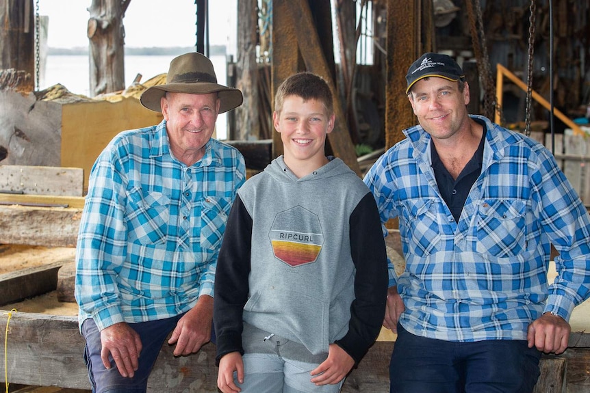 Three generations of Morrison, aged 75 down to 12, smile at the camera in sawmill