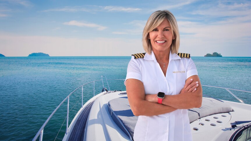 A blonde woman in a boat captains uniform smiles with her arms crossed