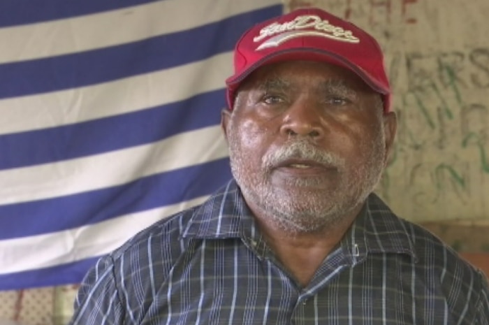 West Papuan asylum seeker Matthew Akari in front of the West Papuan flag.