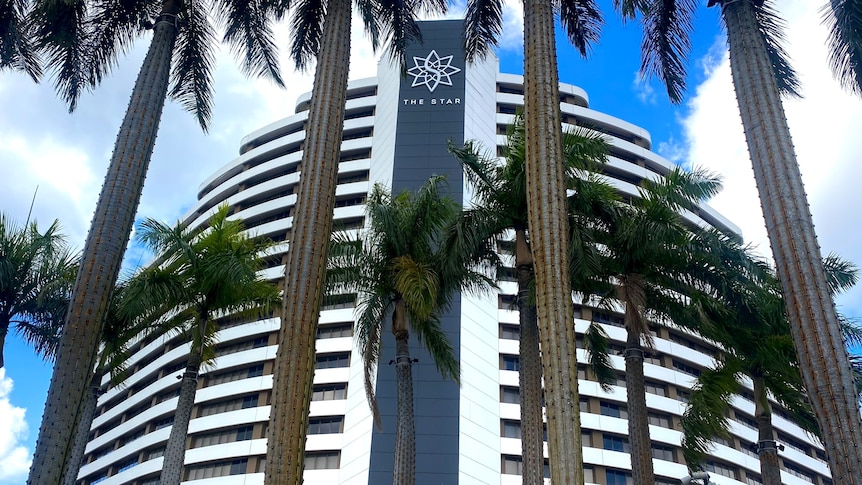 A tall white and black building that says 'The Star' at the top, with tall palm trees in the foreground against blue sky