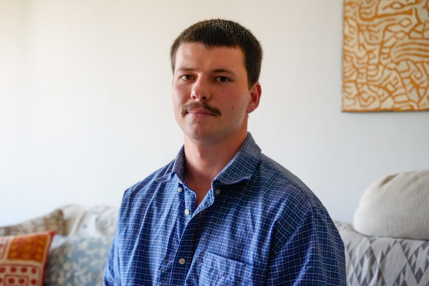 Xavier Sedger poses for a photo in a checked shirt inside his home.
