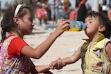 An Iraqi girl helps a young boy drink.