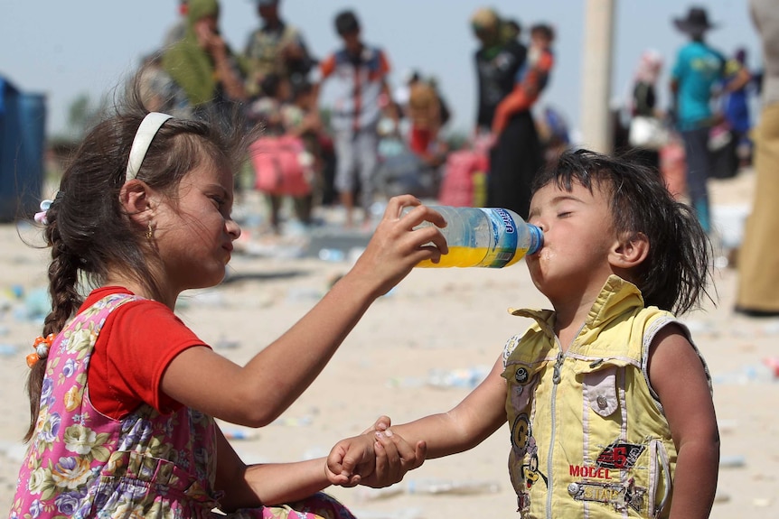 An Iraqi girl helps a young boy drink.