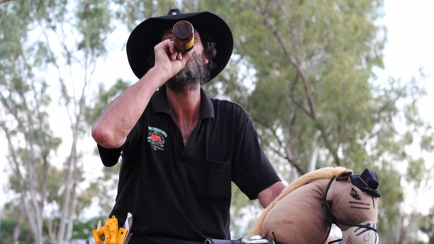 A man on a bicycle drinks from a bottle of beer.