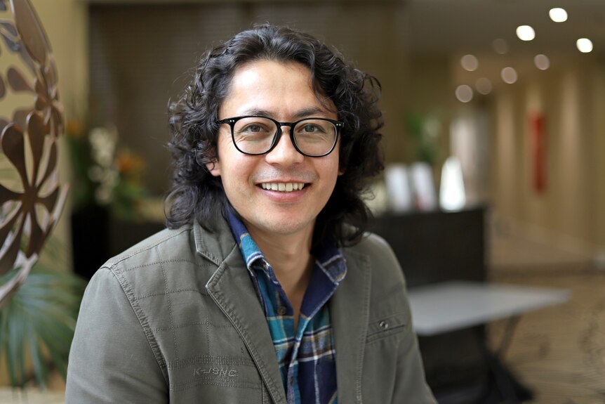 A man with glasses and curly hair smiling to camera