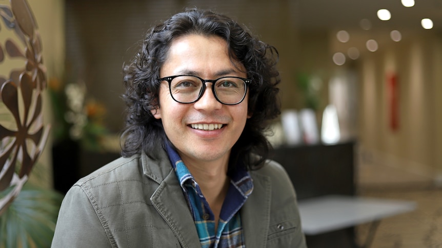 A man with glasses and curly hair smiling to camera