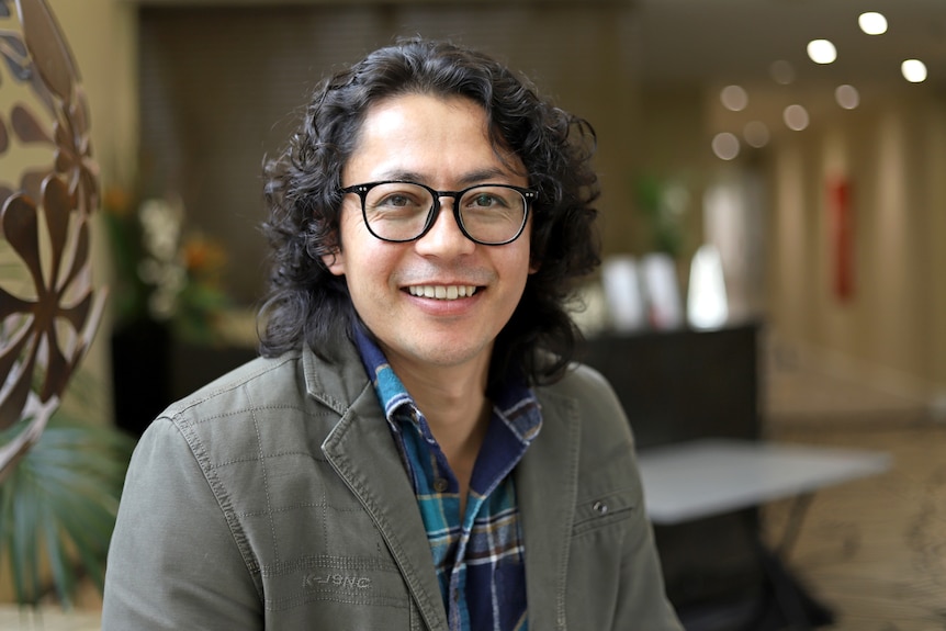 A man with glasses and curly hair smiling to camera