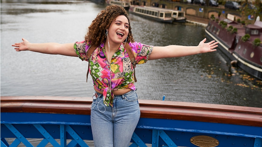 Rose Matafeo mimes a song with her arms outstretched on a bridge over a London canal in Starstruck