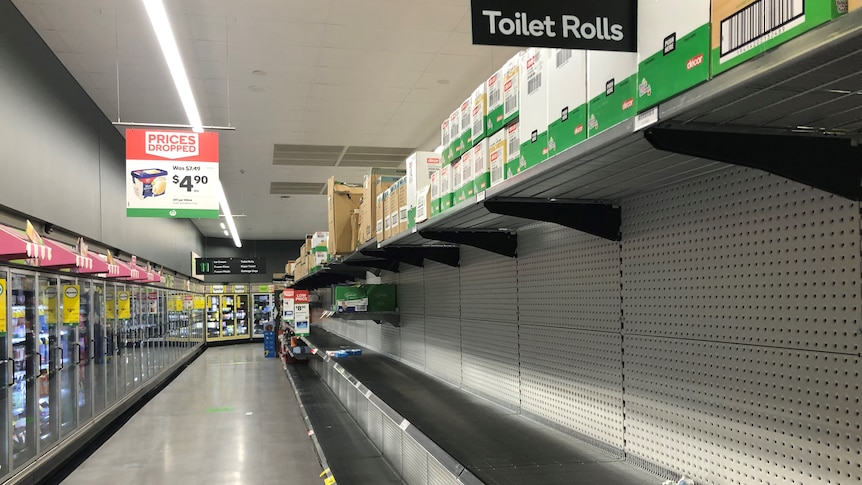 Empty supermarket shelf with a few lonely rolls of toilet paper on it.