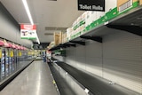 Empty supermarket shelf with a few lonely rolls of toilet paper on it.