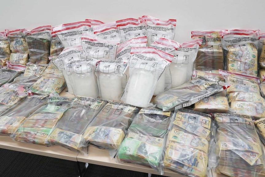 Bundles of cash in sealed plastic bags and jars containing a white substance, also in bags, on a table
