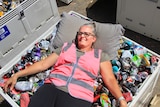Julie Leach lying on top of a container full of cans and bottles, with a pillow.