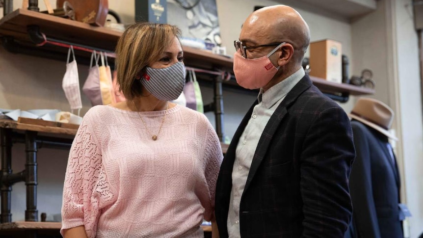 A man and woman pose in masks