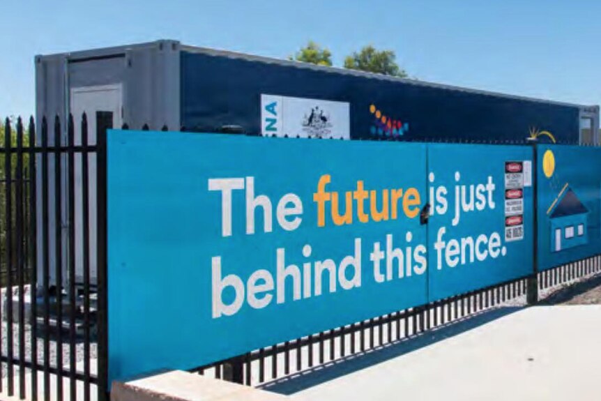 A sea-crate behind a fence hung with a sign reading "The future is just behind this fence"
