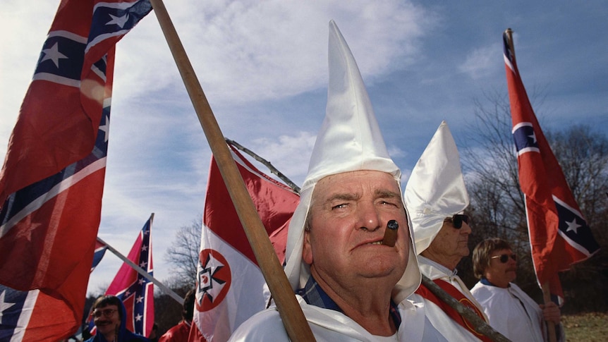 A male member of the Ku Klux Klan smokes a cigar during a rally.