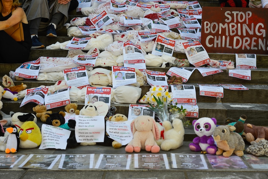 A display of cloths and soft toys with photos of children on steps.