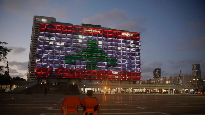 An Israeli rides a bicycle as the municipality building is illuminated with the Lebanese flag In Tel Aviv, Israel.