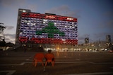 An Israeli rides a bicycle as the municipality building is illuminated with the Lebanese flag In Tel Aviv, Israel.