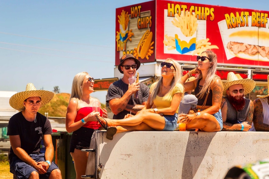 Several people sit on a concrete block at Summernats.