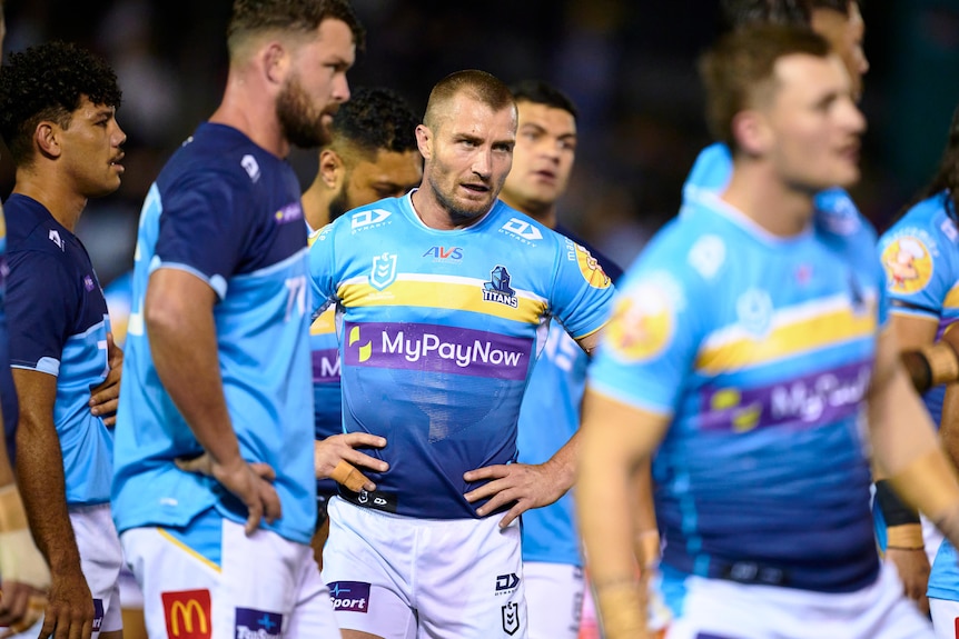 A Gold Coast NRL player stands with hands on hips amongst his teammates before a game.