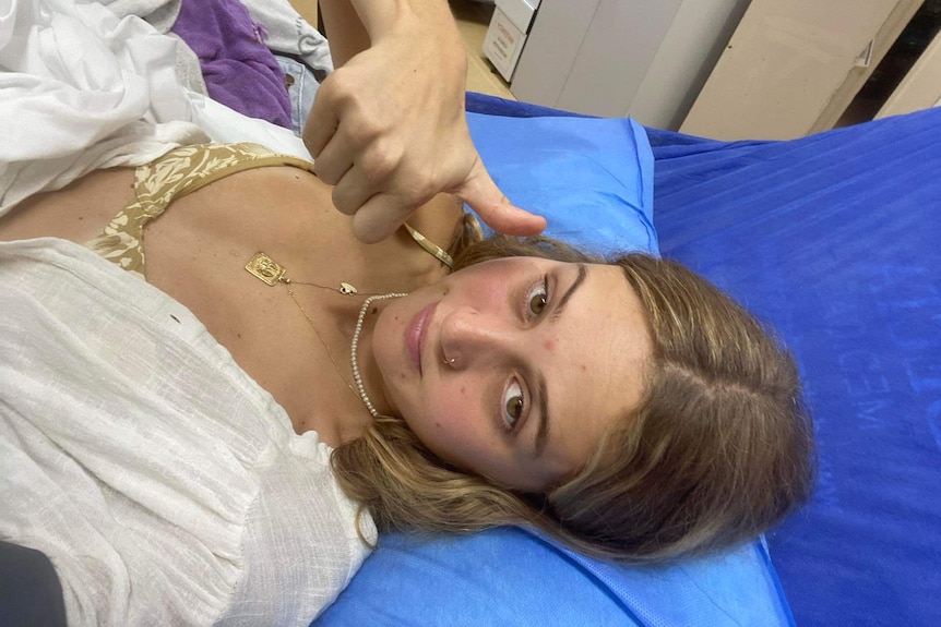 A woman gives a thumbs up while laying on a hospital bed