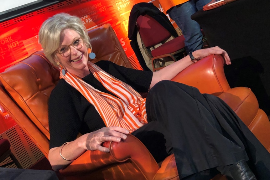 A woman, wearing an orange and white scarf, sits on an orange armchair.