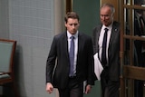 Andrew Hastie mid-stride, with a serious expression on his face, in Parliament.