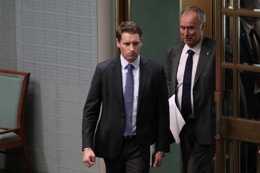 Andrew Hastie mid-stride, with a serious expression on his face, in Parliament.