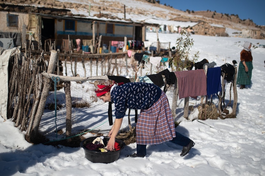 A woman puts clothes to dry amid heavy snowfall outside her home.