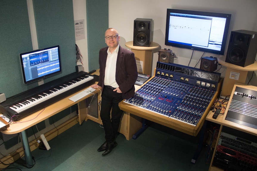 Joe Bennett standing next to a mixing desk and keyboard in a sound studio