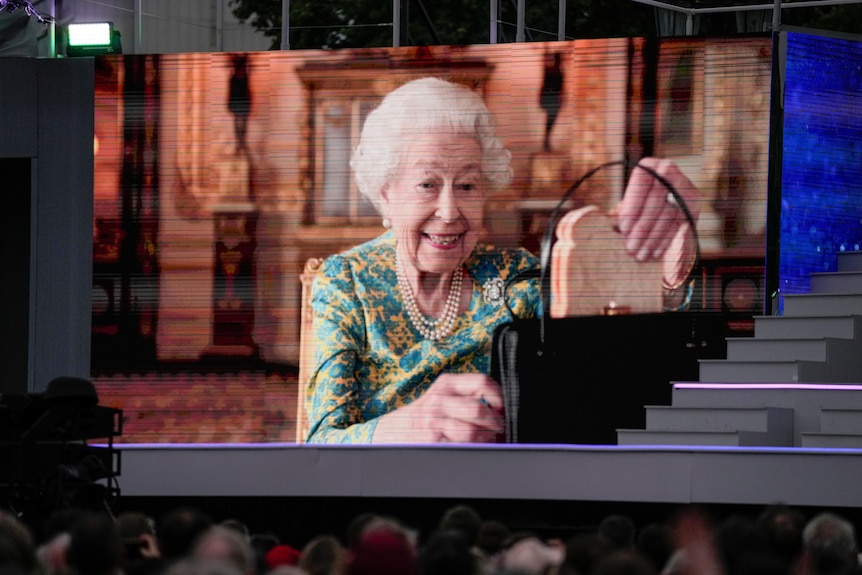 The Queen grins as she takes a sandwich from her handbag