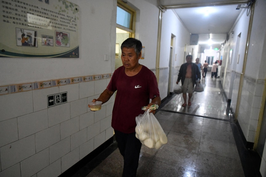 Man walks down hallway carrying breadrolls and donated food. 