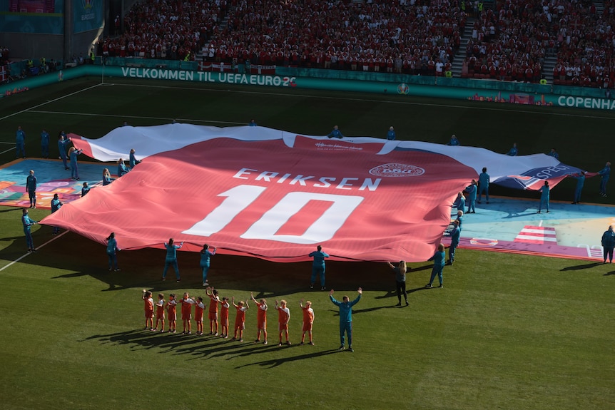 A giant red jersey with "10 Eriksen" written on it is held over a football pitch 