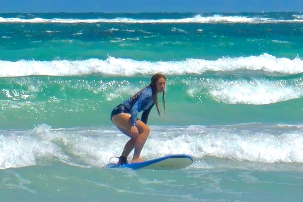 Woman in blue bathers and rashie stand on a surf board