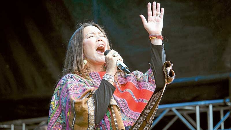 woman singing with left hand raised skywards wearing colourful kaftan