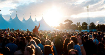 A crowd at Groovin' the Moo music festival where one woman is one another person's shoulders with her arm raised.