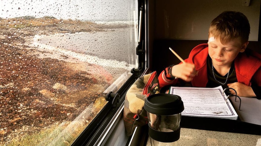 Jake Murphy works on a rainy day on his schoolwork at a table inside the caravan by the sea.