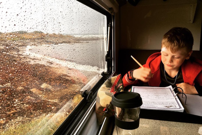 Jake Murphy works on a rainy day on his schoolwork at a table inside the caravan by the sea.