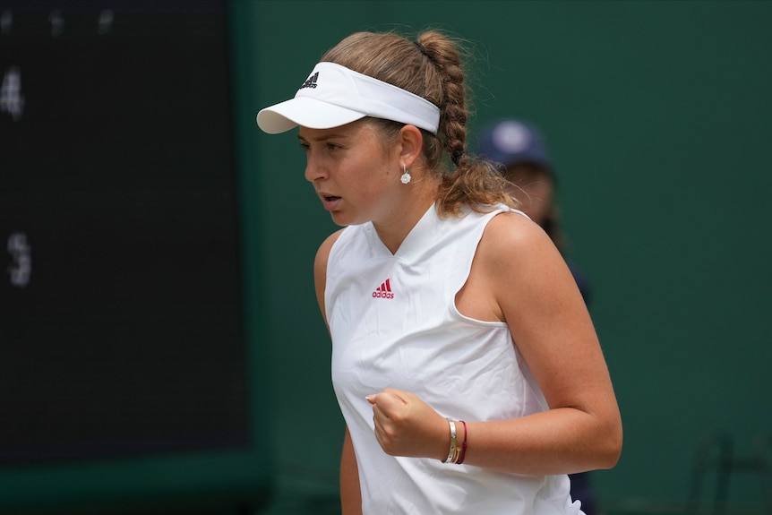 A female tennis player clenches her fist as she stares down the court after winning a point at Wimbledon.
