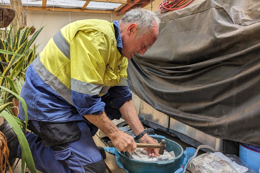 Gerry Lavell pictured from side on smashing plasterboard into a bowl with a hammer. 