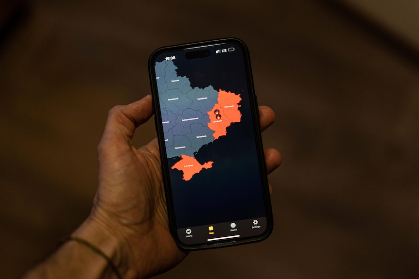 A man's hand holds a smartphone, which is displaying a map of eastern Ukraine. Some segments of the map are highlighted red.