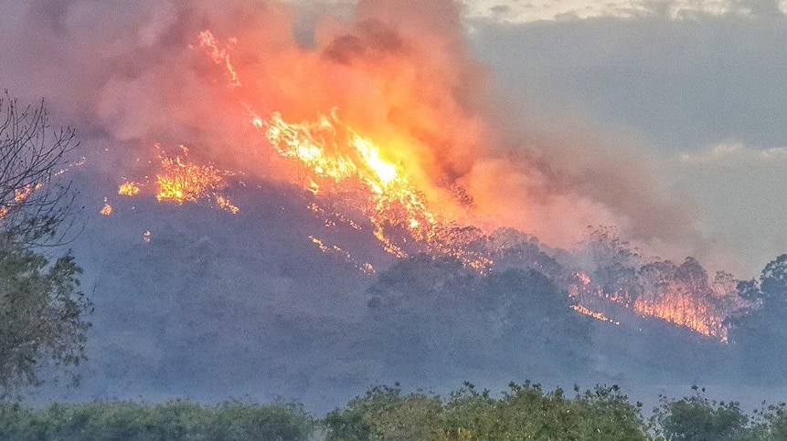 A fire burning trees on a hill in the distance.