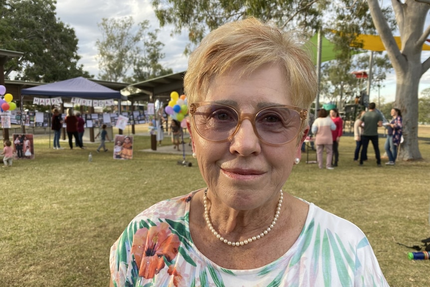 A woman with glasses and a necklace smiles. She has short hair.