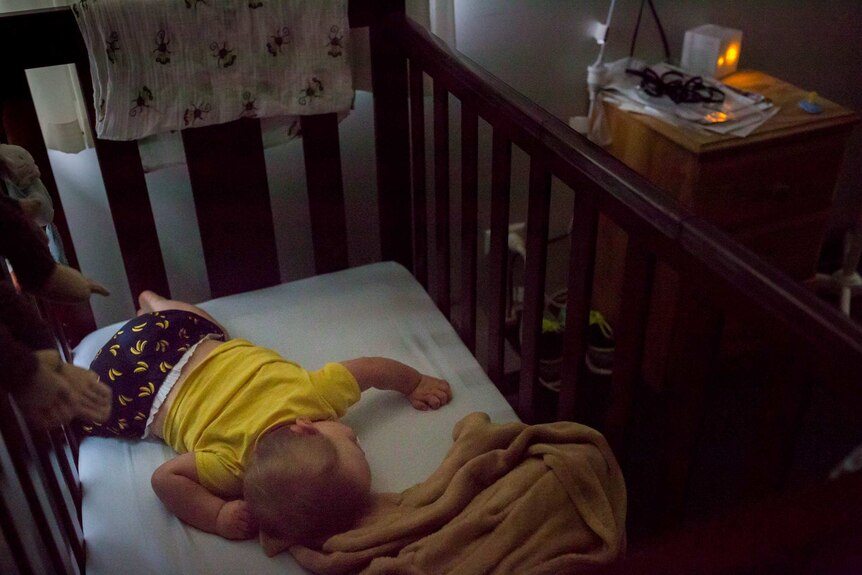 A baby face down in a cot in a darkened room.